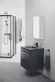 Waschtisch mit schwarzen Griffen und Glasoberfläche, montiert an der Wand. Handtuchhalter an der Wand, Dusche mit Glasabtrennung im Hintergrund. Ideal Standard Produkte.
